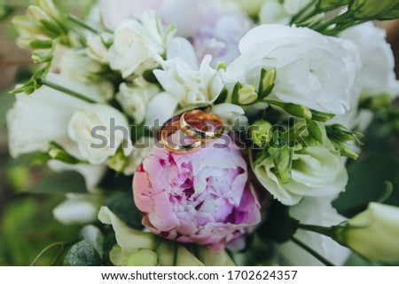 Wedding gold rings lie on a bouquet of white peonies and pink roses close-up. Photography, concept.
