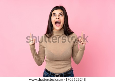 Young woman over isolated pink background surprised and pointing up