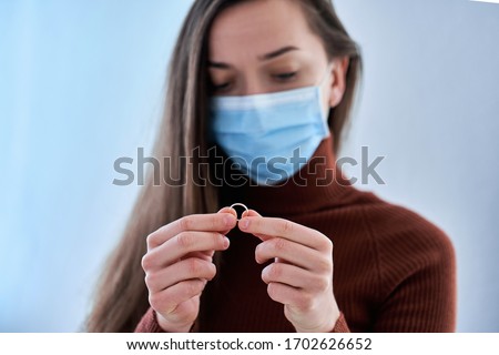 Woman in protective mask holds ring. Break up relationship after living together and staying home with husband during quarantine and isolation due to coronavirus covid epidemic. Divorce concept  Royalty-Free Stock Photo #1702626652