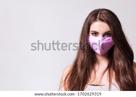 The caucasian girl in pink colored protective face mask. The girl looking at camera. Portrait shot over grey background. virus and pollution protection concept.