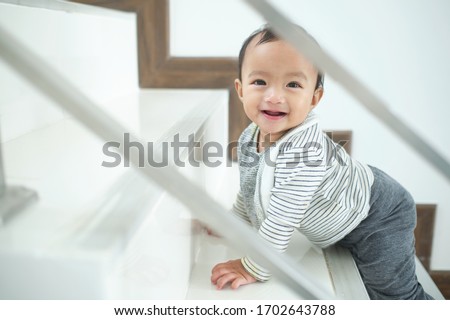 Cute happy Asian 10 months old toddler baby girl child climbing up stairs at home alone, Looking and smiling at camera, Movement, Balance & Coordination, Stair climbing developmental milestone concept Royalty-Free Stock Photo #1702643788