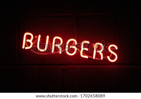 A vintage retro american style neon sign advertising burgers. A dark setting with neon tube lighting up the dark in red. Food advertising and signage in the food industry