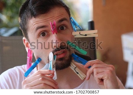 Young Man with many Clothes Pegs Clipped on his Face
