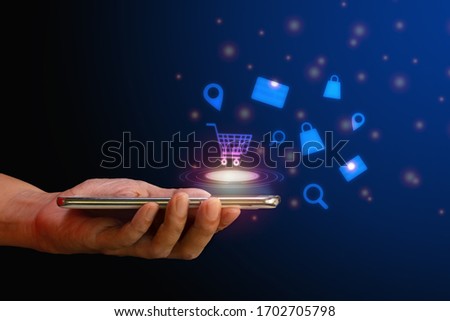 Shop online concept. Hand hold smartphone with shopping cart, search, credit card and bag virtual icon on blue background. Quarantine to save life from corona virus.   Royalty-Free Stock Photo #1702705798