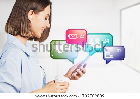 Cheerful young woman with smartphone and coffee standing in blurry white room with bright social media notification icons. Concept of communication and internet. Toned image