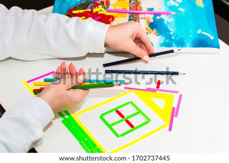 Bright colored rainbow from pencils, a house of bright colored sticks on a white background, made by the hands of a girl