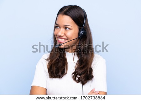 Young telemarketer Colombian woman over isolated blue background looking to the side