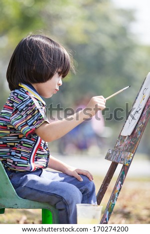 Little European boy painting art board in the park