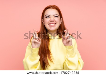 Redhead teenager girl over isolated pink background with fingers crossing