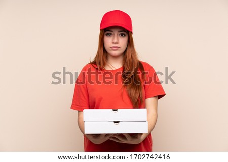 Pizza delivery teenager girl holding a pizza over isolated background keeping arms crossed