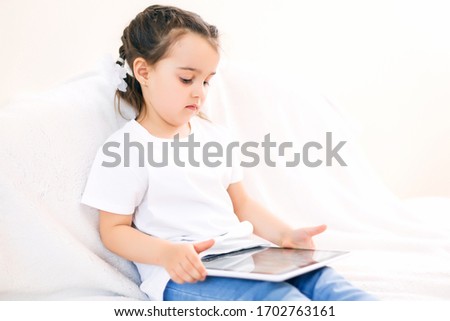Curious little child girl having fun using digital tablet alone sitting on floor, happy preschool smart kid playing with computer looking at screen watching cartoons online at home