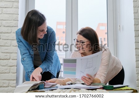 Two women choosing fabrics for curtains. Females textile designer, decorator and client watch palettes with fabrics, choose model and fabric