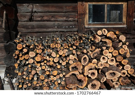 Detail of village life.Cut logs of various sizes for the stove and fire, neatly stacked in a large woodpile against the wall of a sturdy wooden shed with a window and a rusty hook on a nail.Russia