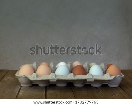 One dozen unwashed colorful chicken eggs in open cartoon on wooden surface side view and plenty of copy-space- free-range eggs of various shapes, colors and sizes very different from commercial eggs 