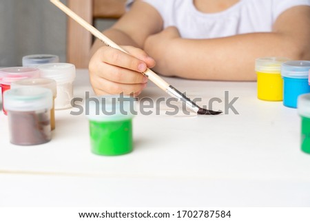 the girl leads with a brush on a white sheet of paper, will paint, stay at home