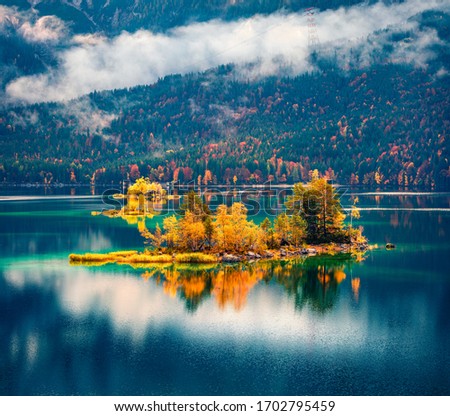 Foggy morning view of Eibsee lake. Picturesque autumn scene of Bavarian Alps, Germany. Colorful mountain hills reflected in the calm surface of water ot pure lake. Beauty of nature concept background.