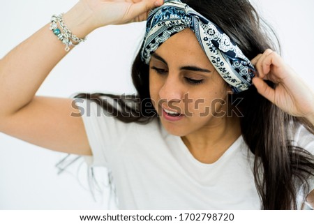 Brunette hippie girl putting a bandana in her hair. White background.