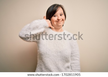 Young down syndrome woman standing over isolated background smiling doing phone gesture with hand and fingers like talking on the telephone. Communicating concepts.