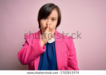 Young down syndrome business woman over pink background asking to be quiet with finger on lips. Silence and secret concept.