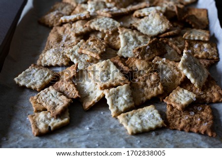 Homemade sea salt and rosemary herbed sourdough crackers fresh out of the oven. The perfect recipe for sourdough discard and baking activities with kids. Flat lay dark food photography. 