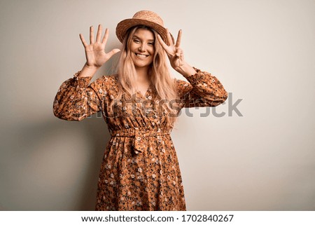 Young beautiful blonde woman wearing summer dress and hat over isolated white background showing and pointing up with fingers number eight while smiling confident and happy.