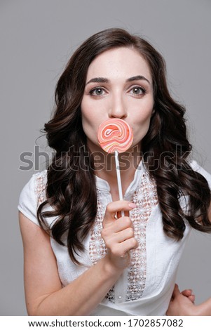 Studio portrait of women with black hair in a white dress. Woman holding colorful lollipop against plain background