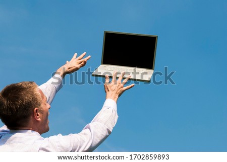 Businessman reaching out to type on laptop computer floating away in blue sky