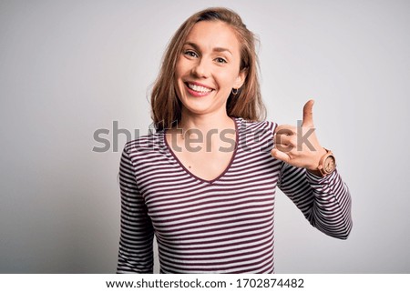 Young beautiful blonde woman wearing casual striped t-shirt over isolated white background doing happy thumbs up gesture with hand. Approving expression looking at the camera showing success.