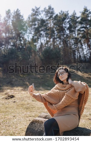 Young attractive stylish girl on the nature on the background of the forest with a phone on a sunny day taking pictures of herself. outdoor holidays and dependence on technology. narcissism.