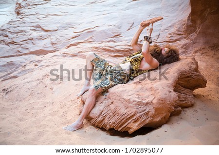 Caveman reclining alone using his primitive stone tablet outdoors in a weathered rock cave