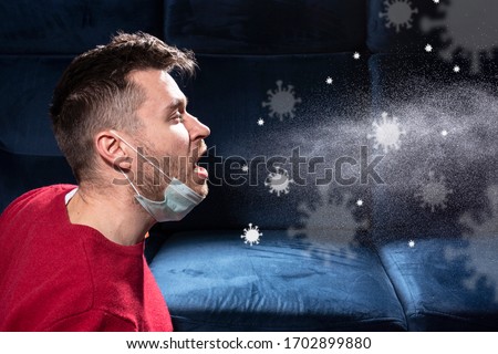 man is coughing. Influenza, cold, coronavirus. Infection through an airborne droplet. A guy in a red sweater and a medical mask is coughing. Visible coronavirus particles in the air. Royalty-Free Stock Photo #1702899880