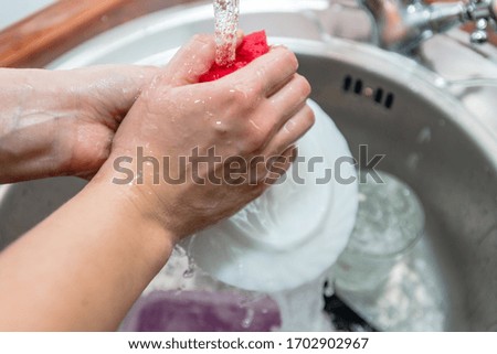 Close up woman's hands of washing dishes in kitchen sink. Cleaning chores