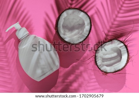 Minimalistic beauty still life. Two halves of chopped coconut and white bottle of cream with shadows from palm leaves on pink background. Creative fashion concept. Top view.