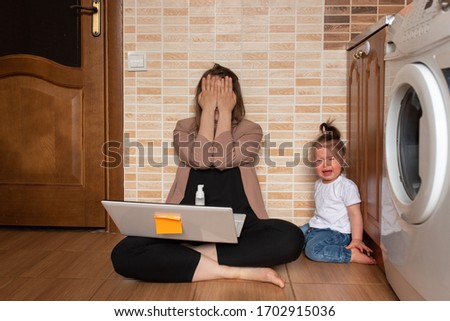 Young beautiful mother is trying to work remotely. Her little daughter is bothering her. Royalty-Free Stock Photo #1702915036
