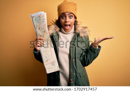 African american skier tourist girl wearing snow sportswear and ski goggles holding city map very happy and excited, winner expression celebrating victory screaming with big smile and raised hands