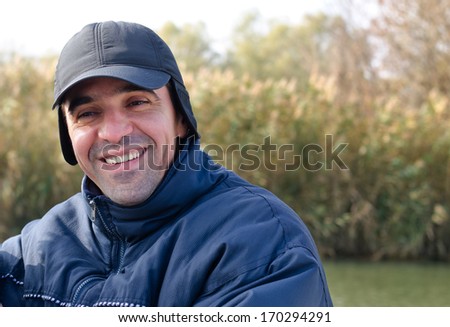 Happy man with a wide friendly smile wearing a blue cap and warm clothing, close up head and shoulders view
