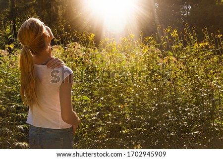 View of a beautiful long hair blonde woman in garden rejoices sunset in nature. 
