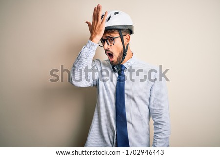 Young businessman wearing glasses and bike helmet standing over isolated white bakground surprised with hand on head for mistake, remember error. Forgot, bad memory concept.