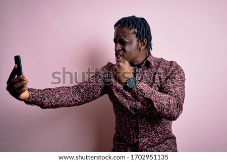 Young handsome african american man wearing casual shirt standing making selfie by camera annoyed and frustrated shouting with anger, crazy and yelling with raised hand, anger concept