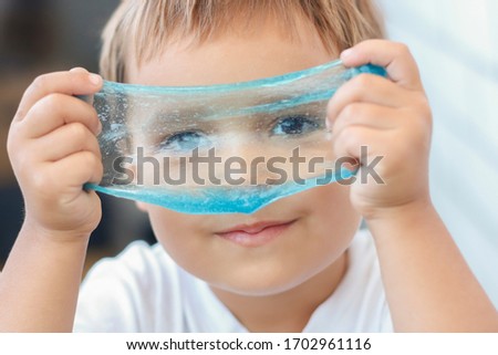Funny girl holding a glitter slime in front of her face and looking through its hole