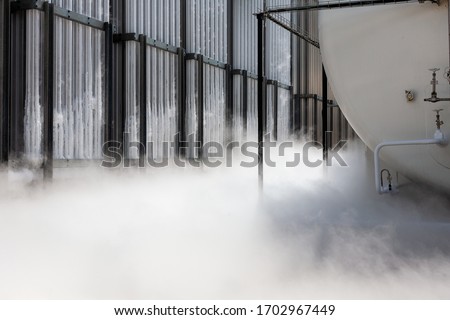 Gasifier turns compressed natural gas from liquid form to gas, condensed frozen pipes release cold white mist Royalty-Free Stock Photo #1702967449