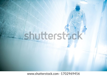 corona virus concept. male scientist doctor in latex biochemical protective suit walking in laboratory coridor holding children plush toys