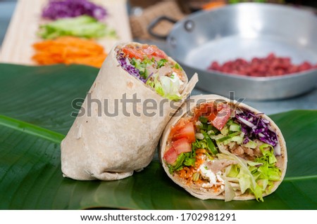 Close up vegetarian burrito wrap vegetables on a banana leaf sliced in half. Tomatoes, cucumber, soy meat, lettuce, purple cabbage carrots Royalty-Free Stock Photo #1702981291