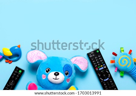 Black TV audio remote control and baby toys rattles, toy puppy on blue background flat lay top view copy space. Concept of viewing children's television shows, cartoons, children's films. Home leisure