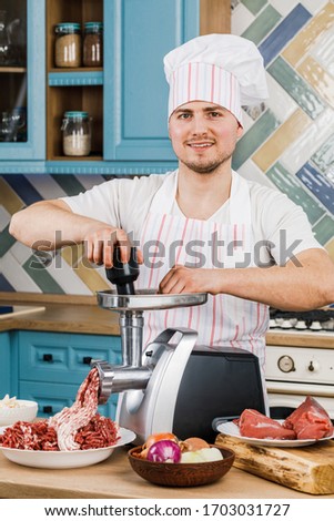 Raw meat. The process of preparing minced meat is carried out using a meat grinder. A male chef uses a meat grinder in the kitchen