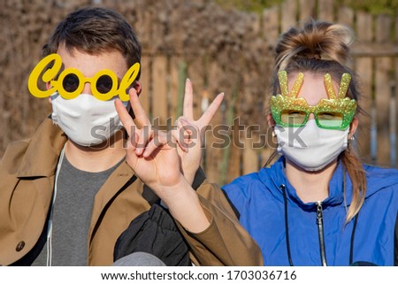 Two teenagers, a young man and a girl, in protective medical masks and funny glasses, make gestures that everything will be fine. Support during the covid-2019 coronavirus epidemic.Focus on the hands.