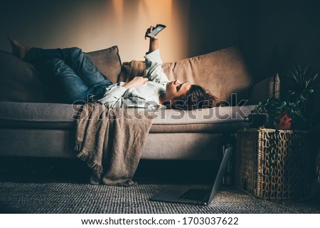 Bored woman in self isolation laying on the sofa. Woman in quarantine for coronavirus working from home. Royalty-Free Stock Photo #1703037622