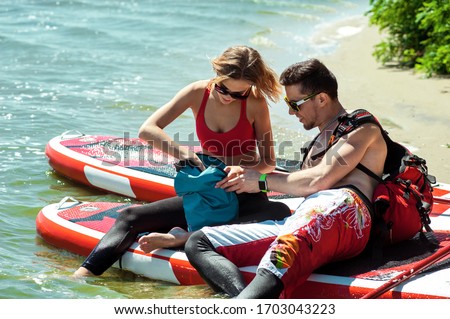 Young athletic couple resting on the riverbank. He takes out his food and water from a backpack.
