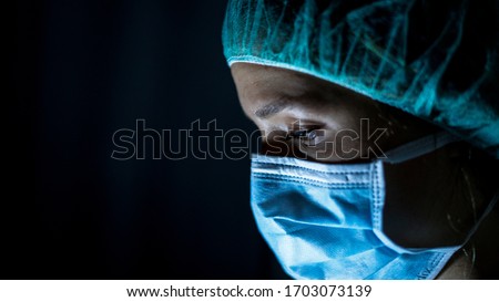 Portrait of young female surgeon, wearing mask and a surgical mask, in front of black background Royalty-Free Stock Photo #1703073139