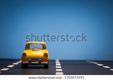 Front view of a Yellow toy car on a blue background and on an asphalt road.